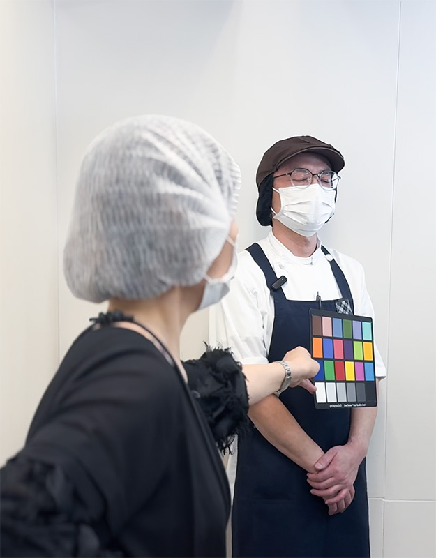 撮影現場でカラーチェッカーを持つU-MAスタッフと、撮影に協力するメンバー